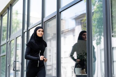 Binaya yakın koşan tesettürlü ve spor kıyafetli Arap kadın. 