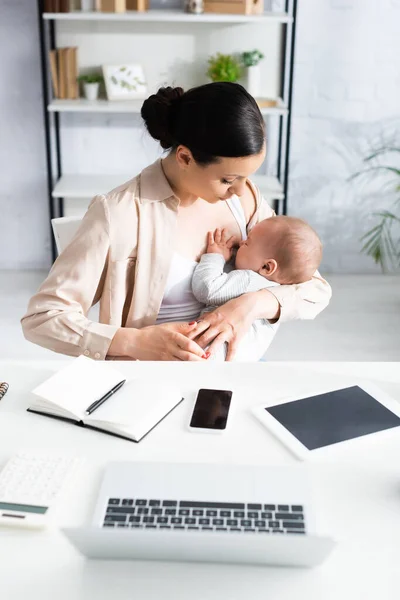 Madre Amamantando Lindo Bebé Hijo Cerca Gadgets Mesa —  Fotos de Stock