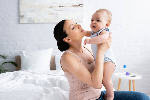 beautiful mother looking at cute infant son in bedroom