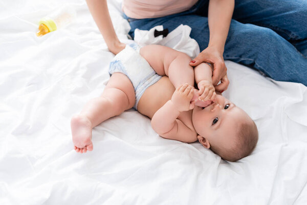 мать сидит на кровати и трогает милого младенца сына в подгузнике
 