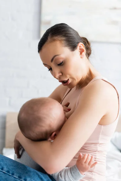 ベッドルームで母乳育児をしながら幼児を見ている感情的な母親 — ストック写真