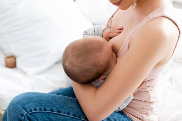 cropped view of mother breastfeeding infant son in bedroom 