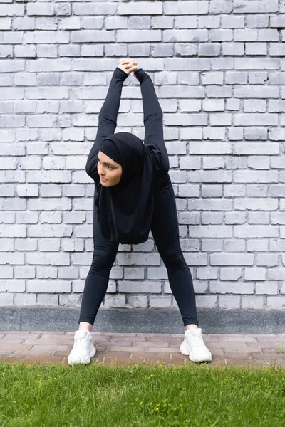 年轻的穆斯林女运动员在砖墙和绿草附近锻炼 — 图库照片