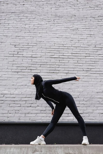 阿拉伯女运动员戴头巾在砖墙附近锻炼的侧视图 — 图库照片