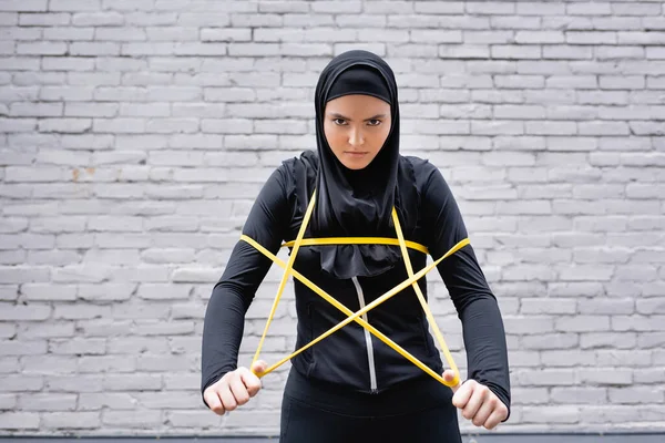 阿拉伯女运动员头戴头巾 带着抵抗带在砖墙边锻炼 看着镜头 — 图库照片