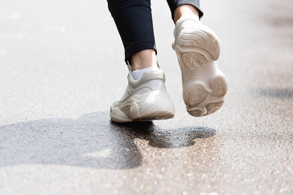 cropped view of sportswoman in white sneakers running outside 