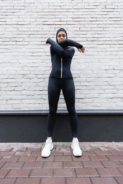 穿着头巾和运动服的穆斯林女运动员在砖墙附近锻炼 — 图库照片