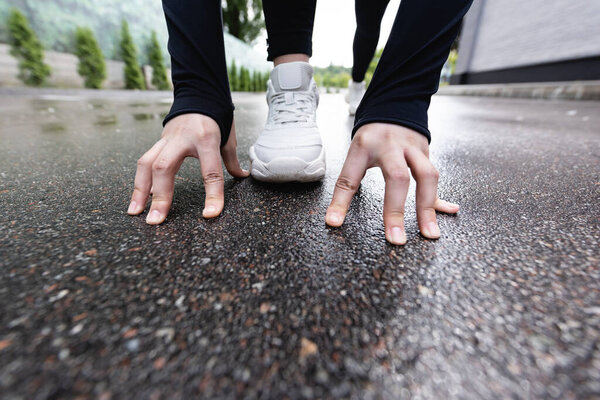 selective focus of runner in white sneakers standing in starting pose outside 