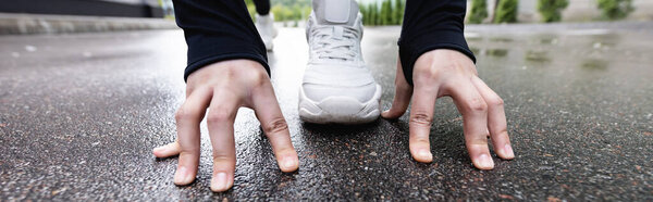 horizontal crop of runner in white sneakers standing in starting pose outside 