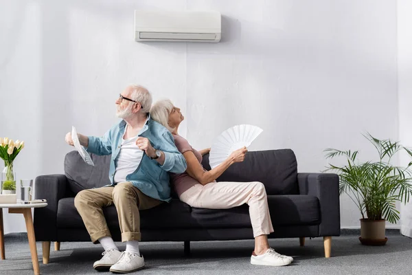 Senior Man Håller Tidningen Nära Trött Fru Med Fläkt Luftkonditionering — Stockfoto