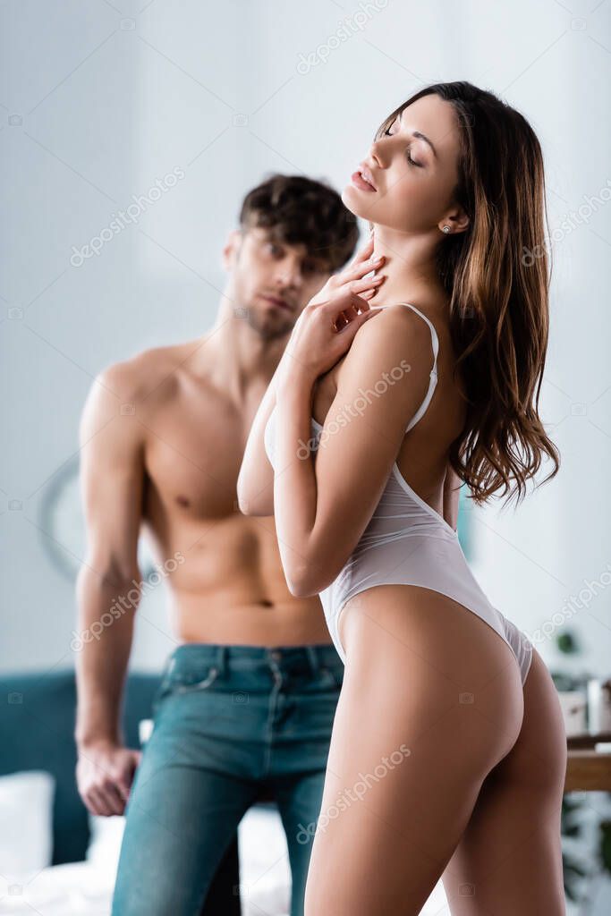 Selective focus of passionate girl in bodysuit touching neck near shirtless boyfriend 