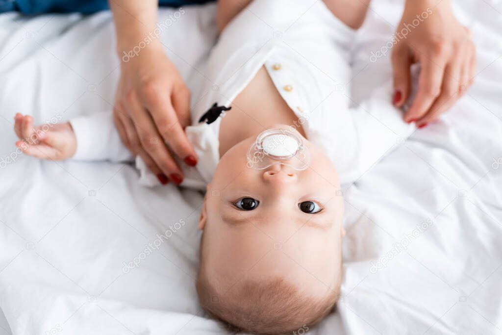 overhead view of mother wearing baby romper on infant boy with pacifier