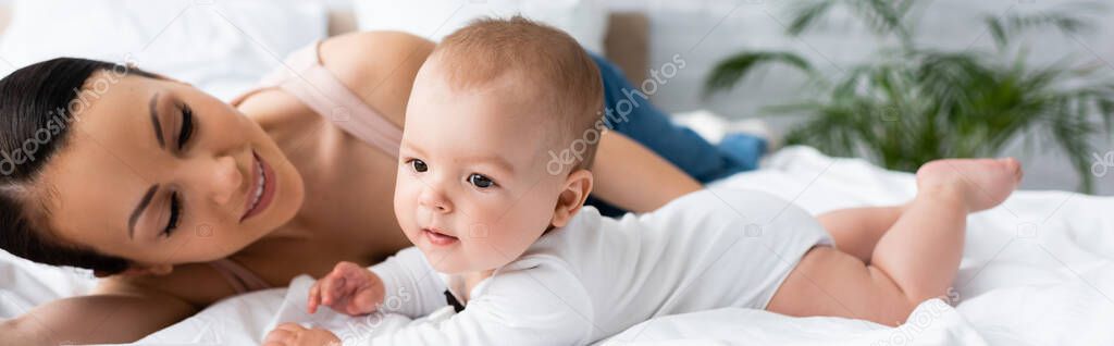 website header of happy mother looking at barefoot infant son on bed