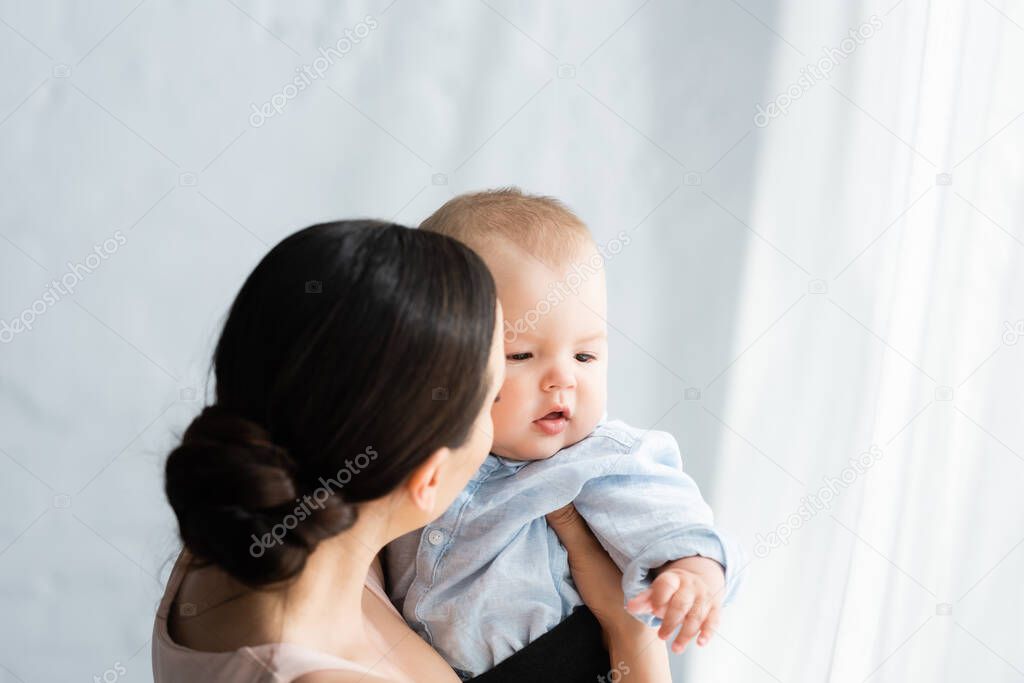 mother holding in arms cute infant son in baby clothing 