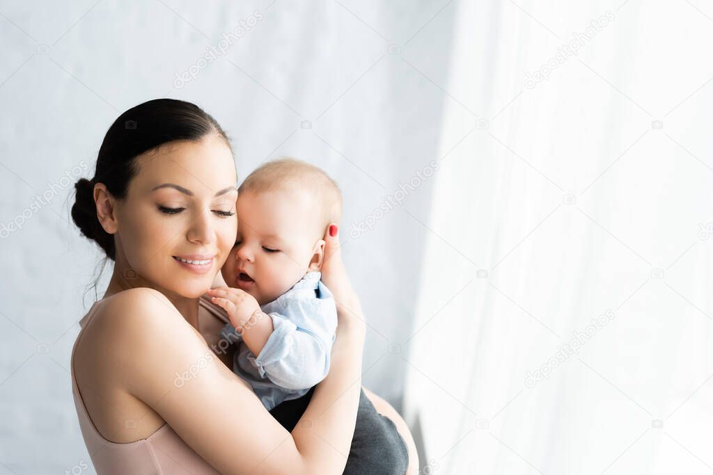happy mother holding in arms cute infant son in baby clothing 