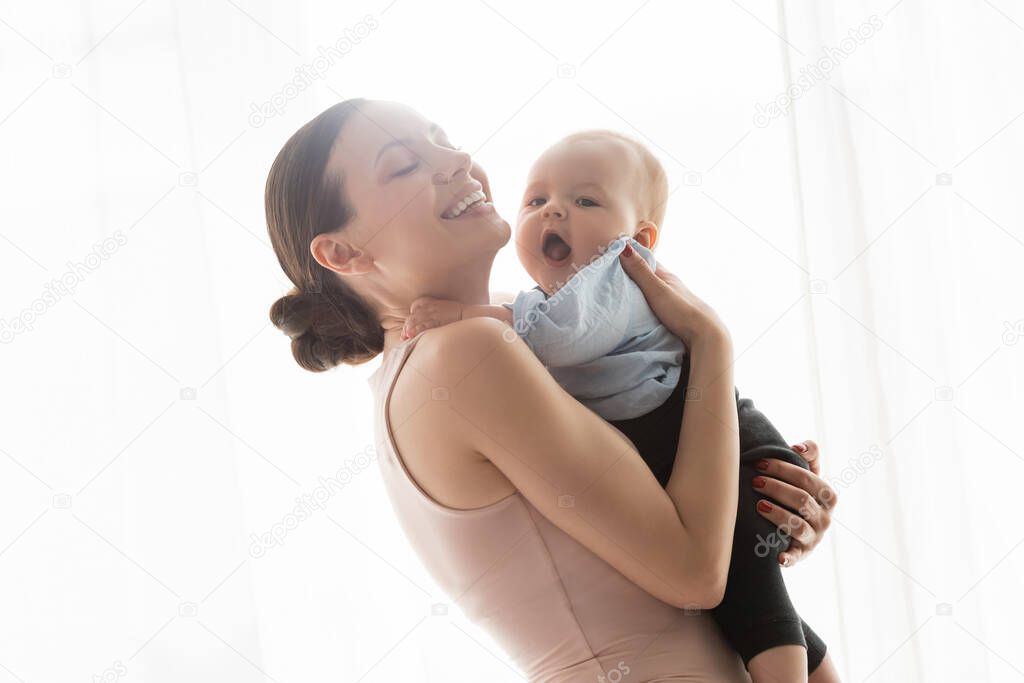 smiling mother with closed eyes holding in arms infant son in baby clothing 
