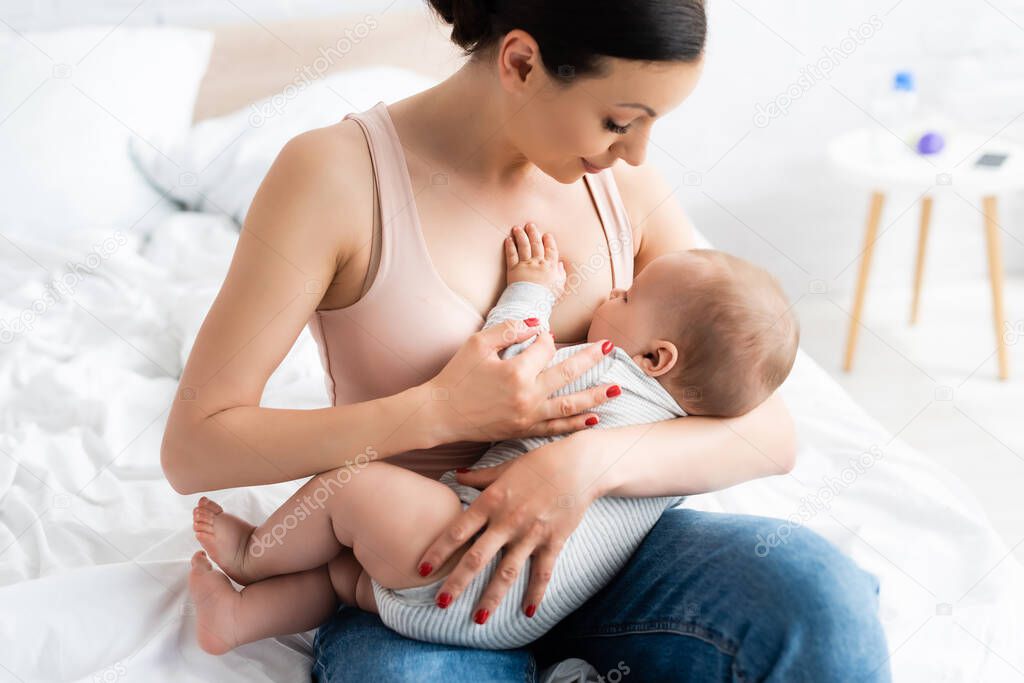 caring mother breastfeeding baby boy in bedroom 