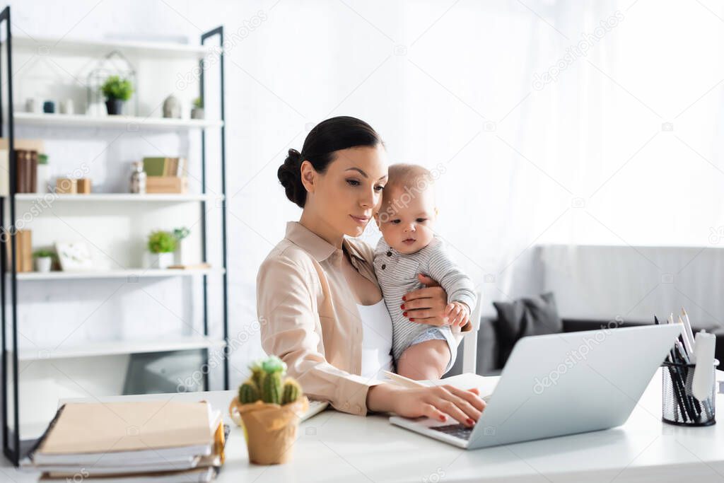 selective focus of attractive mother holding in arms baby boy and working from home