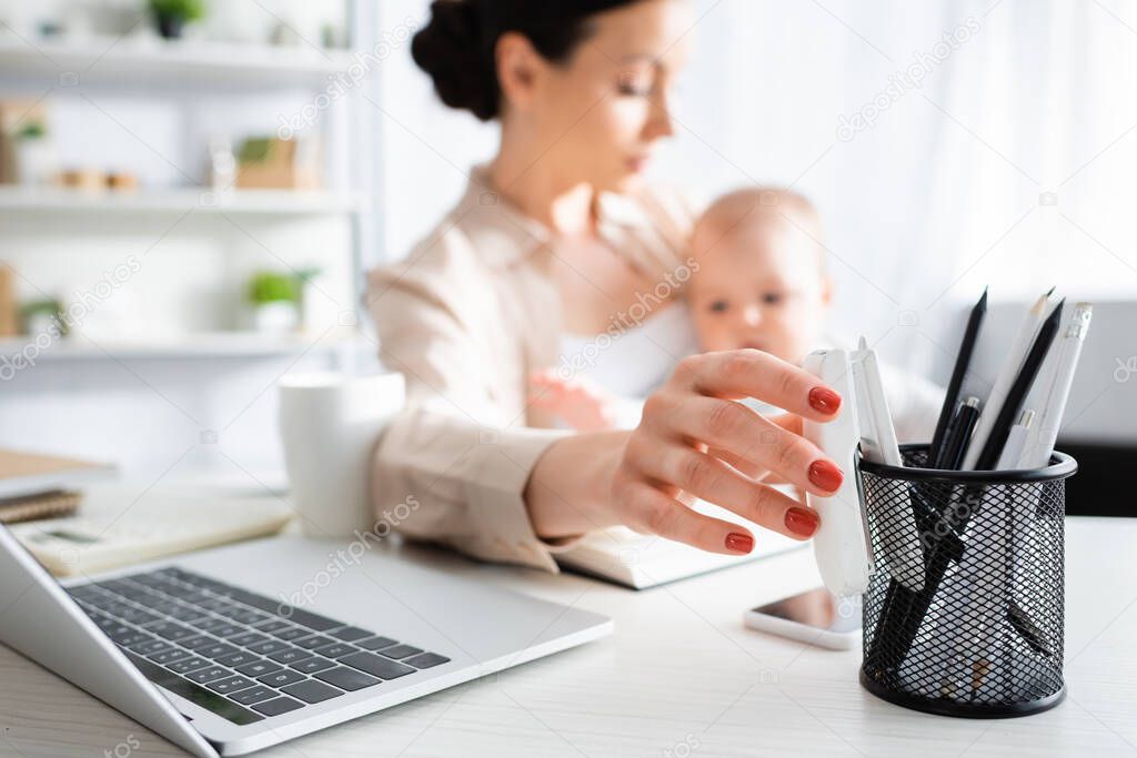 selective focus of mother reaching stationery while holding in arms cute infant son 