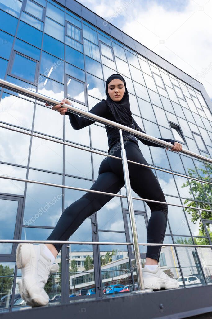low angle view of arabian woman in hijab holding handrail while working out near modern building 