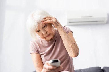 Isıdan muzdarip yaşlı bir kadının seçici odak noktası ve klimanın uzaktan kumandasını elinde tutuyor 