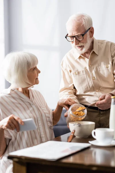 Selective Focus Smiling Woman Holding Smartphone Husband Jar Cereals Kitchen — Stock Photo, Image