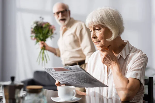 Selective Focus Senior Woman Reading Newspaper Positive Husband Bouquet — Stock Photo, Image
