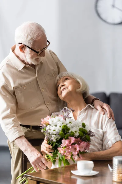 Επιλεκτική Εστίαση Του Ηλικιωμένου Άνδρα Αγκαλιάζει Χαμογελαστή Σύζυγο Μπουκέτο Κοντά — Φωτογραφία Αρχείου