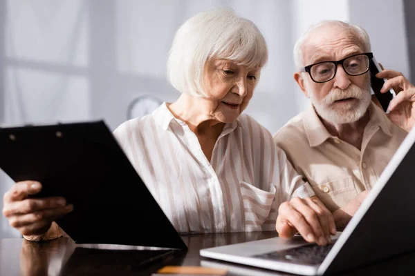 Selective Focus Senior Woman Holding Clipboard Using Laptop Husband Talking — Stock Photo, Image