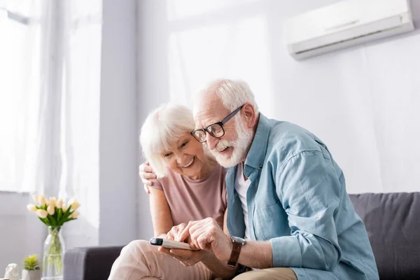 Positive Senior Couple Using Remote Controller Air Conditioner Sofa — Stock Photo, Image