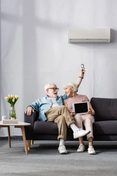 自宅でエアコンのデジタルタブレットとリモートコントローラーを保持している笑顔のシニアカップル — ストック写真