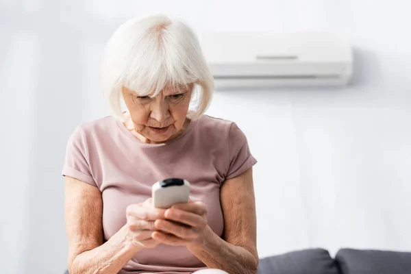 Selektivt Fokus För Äldre Kvinna Som Håller Fjärrkontroll Luftkonditioneringen Hemmet — Stockfoto