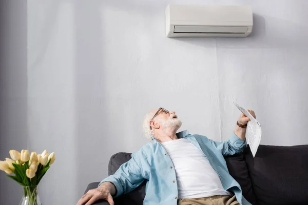 老年人拿着报纸 看着家里的空调机的选择性焦点 — 图库照片