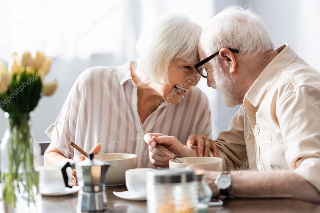 Selective focus of positive senor couple looking at each other near coffee and breakfast on table 