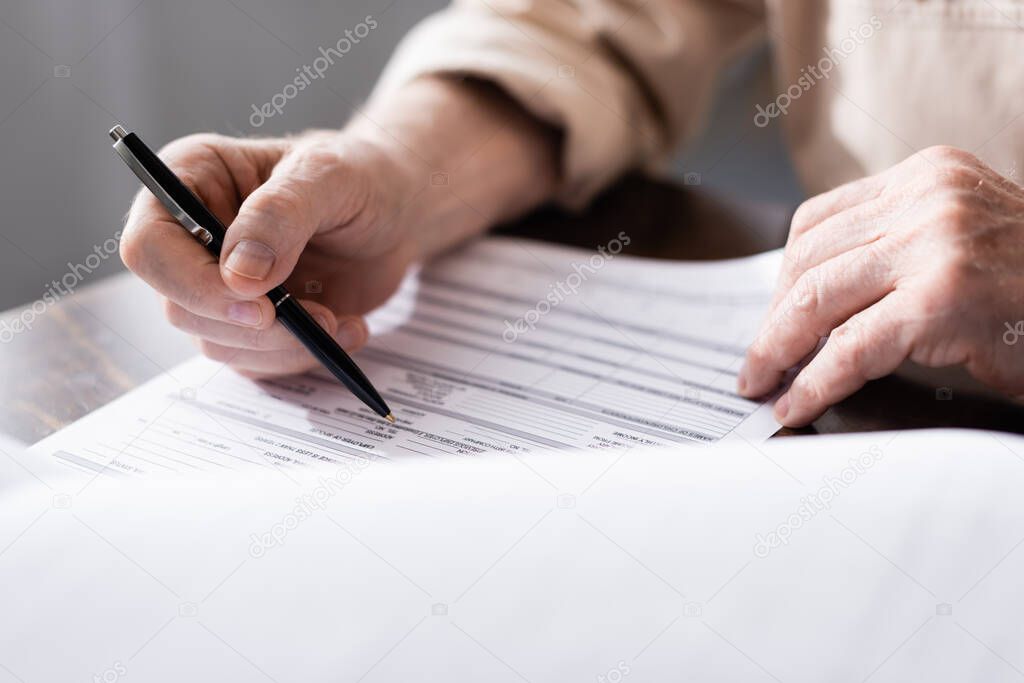 Cropped view of senior man holding pen near papers on table 
