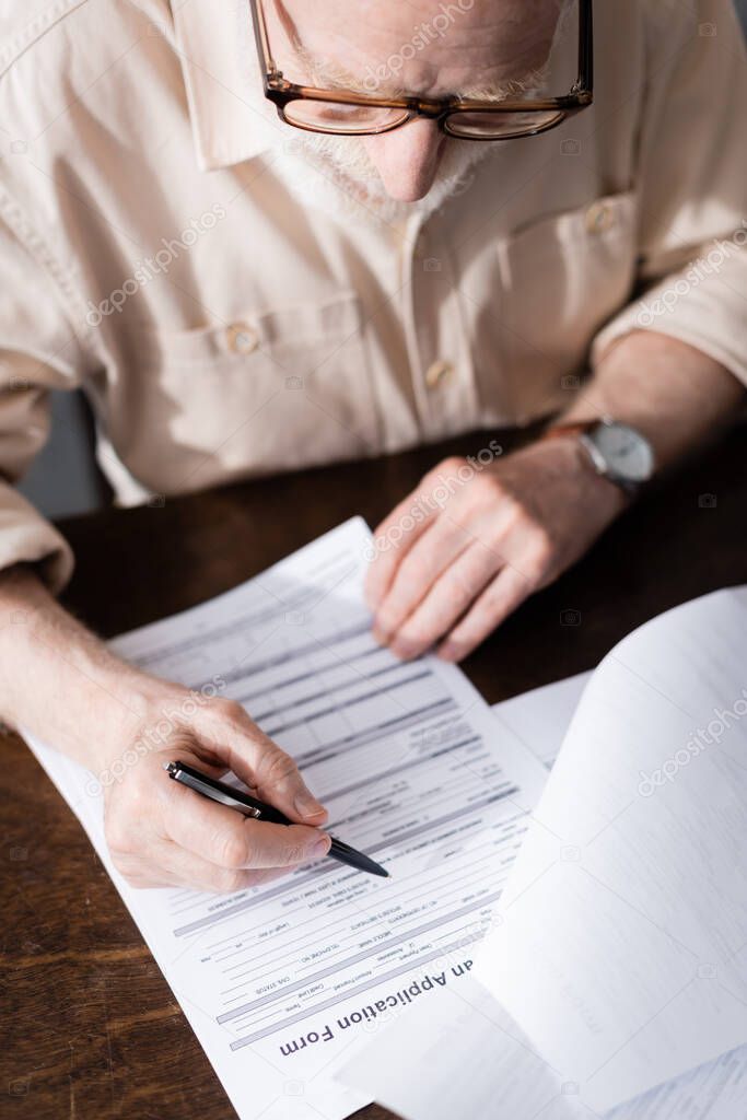 Selective focus of elderly man in eyeglasses writing on papers at table 