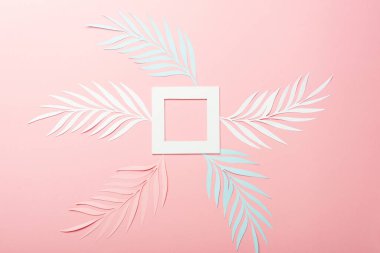 Pembe arka planda beyaz, pembe ve mavi kağıt kesim palmiye yaprakları ve kare çerçeve üst görünüm