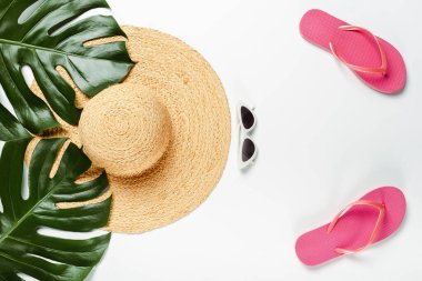 Yeşil palmiye yapraklarının üst görünümü, hasır şapka, güneş gözlükleri ve beyaz arkaplanda parmak arası terlikler