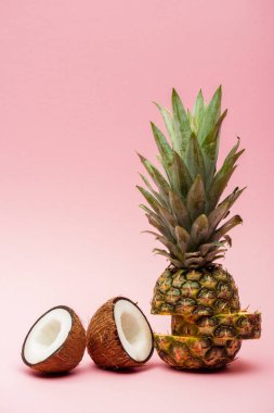 Pembe arka planda olgun ananas ve taze hindistan cevizi yarıları.