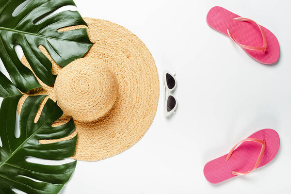 top view of green palm leaves, straw hat, sunglasses and flip flops on white background