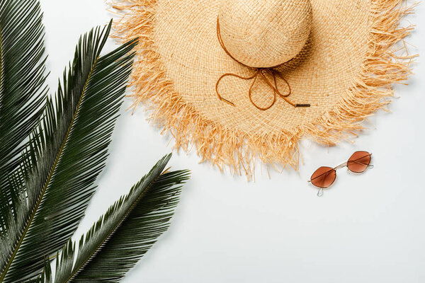 top view of green palm leaves, straw hat and sunglasses on white background