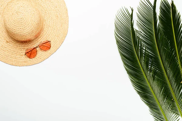 top view of green palm leaves near straw hat and sunglasses on white background