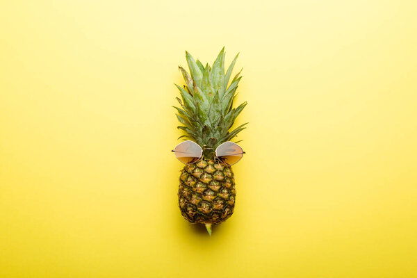 top view of ripe pineapple in sunglasses on yellow background