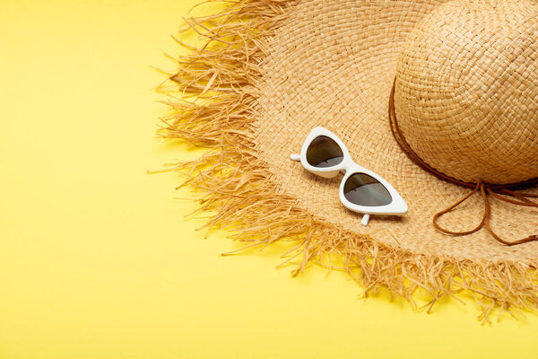 straw hat and stylish suglasses on yellow background