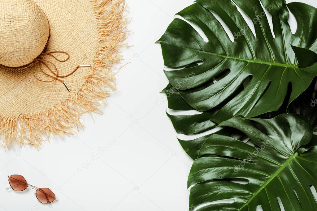 top view of green palm leaves, straw hat, sunglasses on white background