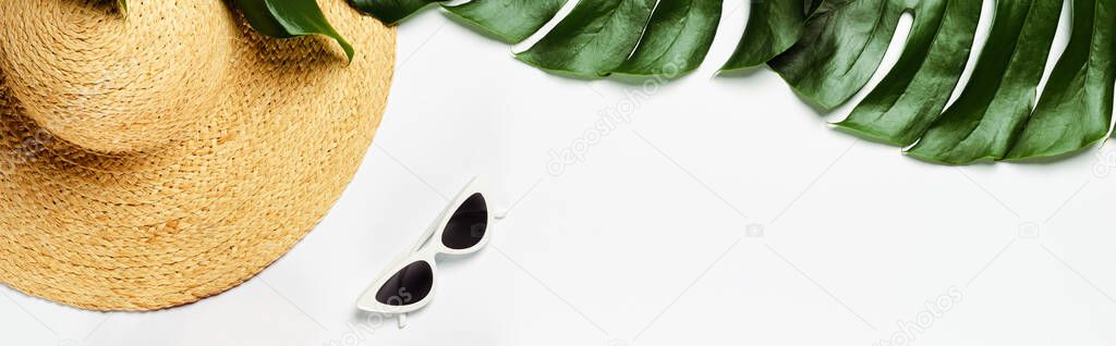 top view of green palm leaves, straw hat and sunglasses on white background, panoramic shot