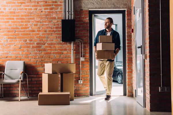 handsome man holding carton boxes while walking in new office 