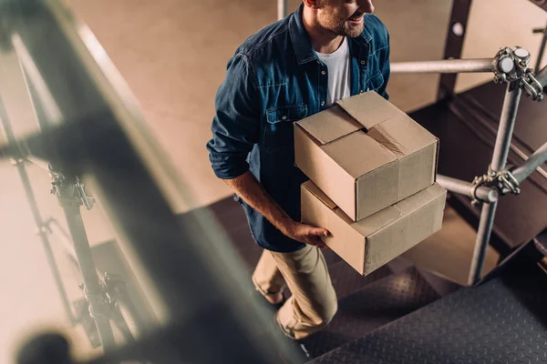 cropped view of positive businessman holding boxes and walking on stairs in new office