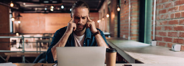 panoramic crop of pensive businessman looking at laptop in office