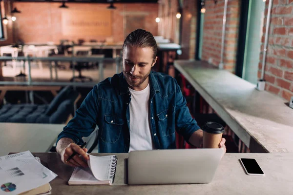 Alegre Hombre Negocios Mirando Cuaderno Sosteniendo Taza Papel Cerca Teléfono —  Fotos de Stock